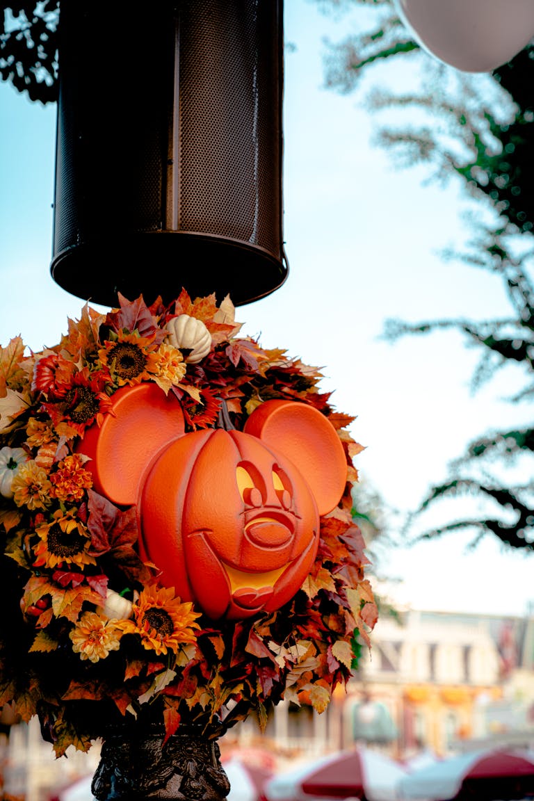 A festive Mickey Mouse pumpkin decoration surrounded by fall leaves, perfect for Halloween celebrations.