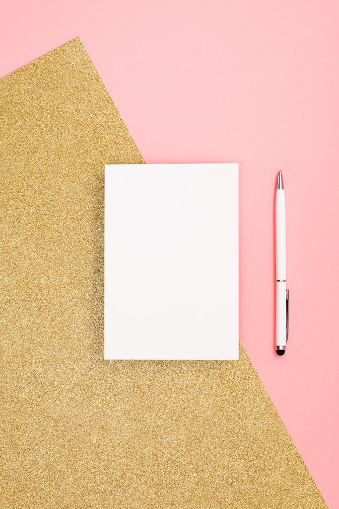 A stylish flat lay featuring a blank notepad and pen on a pink and gold glitter surface.